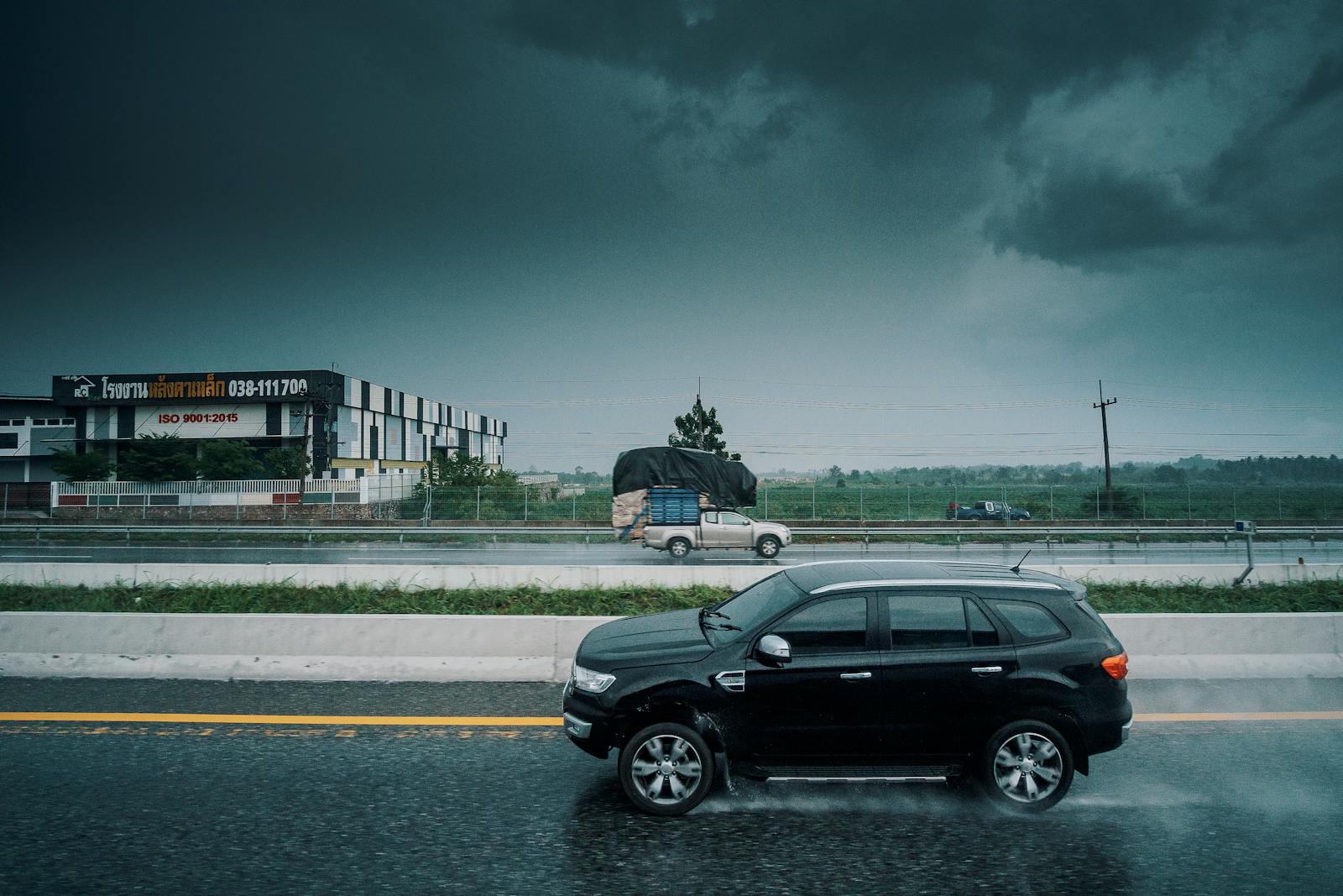 Black SUV travels on a rainy highway, showcasing stormy weather and transportation dynamics.