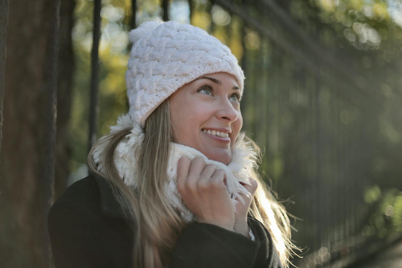 A joyful woman in a knit hat and scarf enjoying a sunny winter day outdoors.