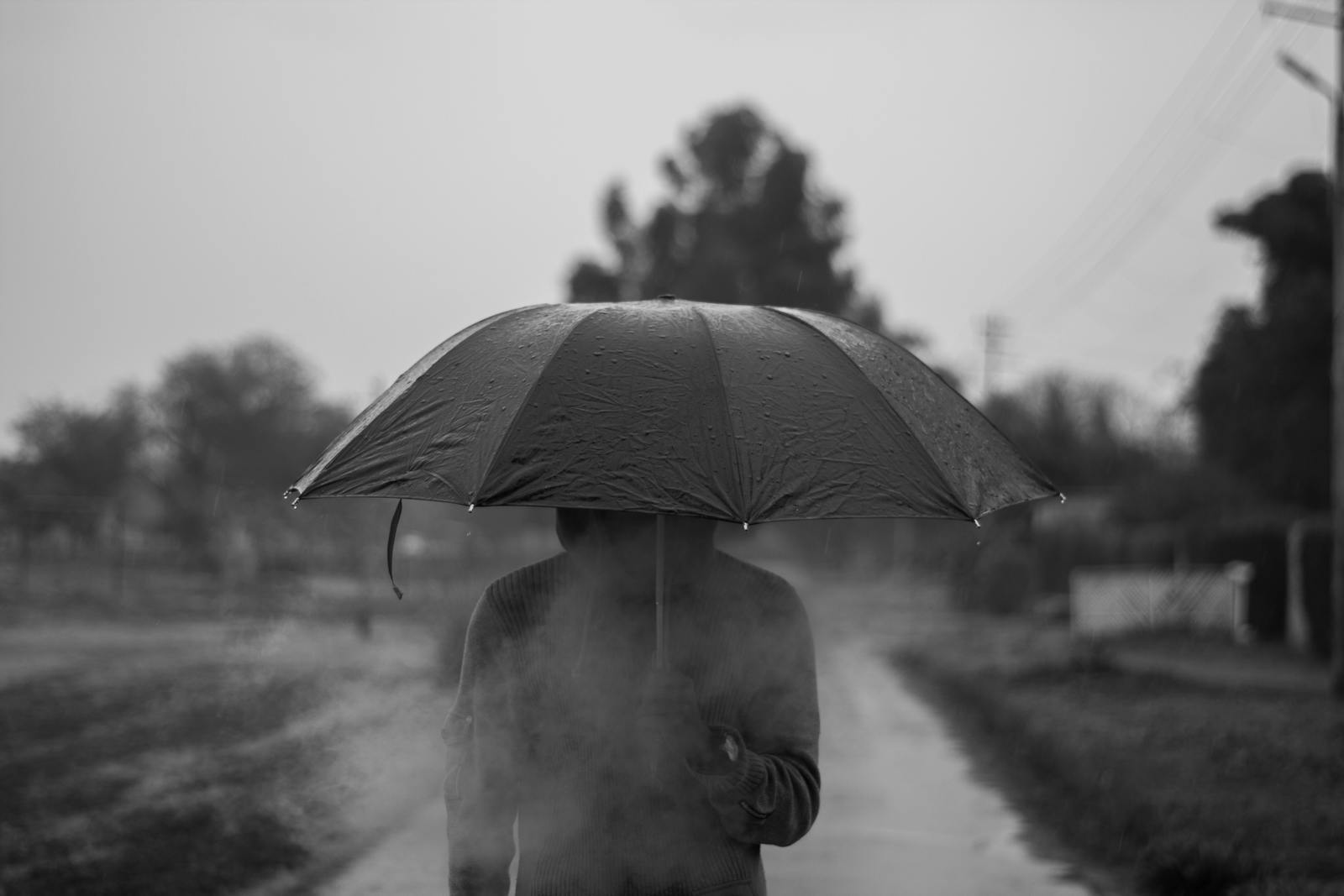 Moody black and white image of a person holding an umbrella in the rain, creating a mysterious silhouette with smoke.