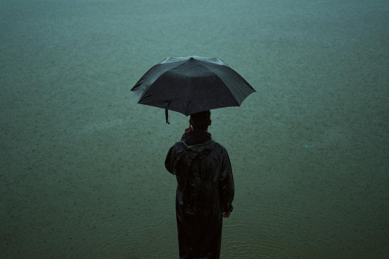 A person stands alone in the rain, holding an umbrella, creating a moody atmosphere.