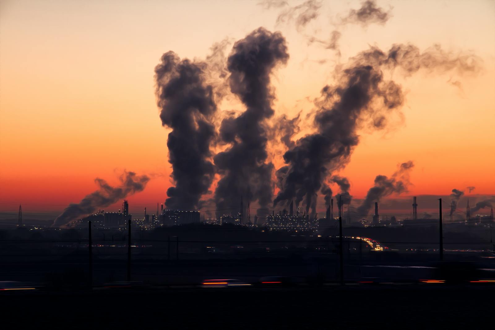 Silhouette of a factory with smoke emissions against a vibrant sunset sky.