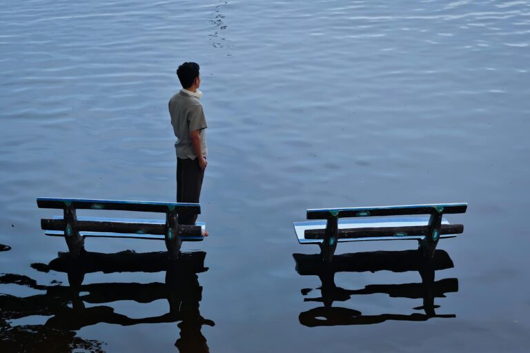 A man stands between benches in a flooded area, creating a contemplative scene.