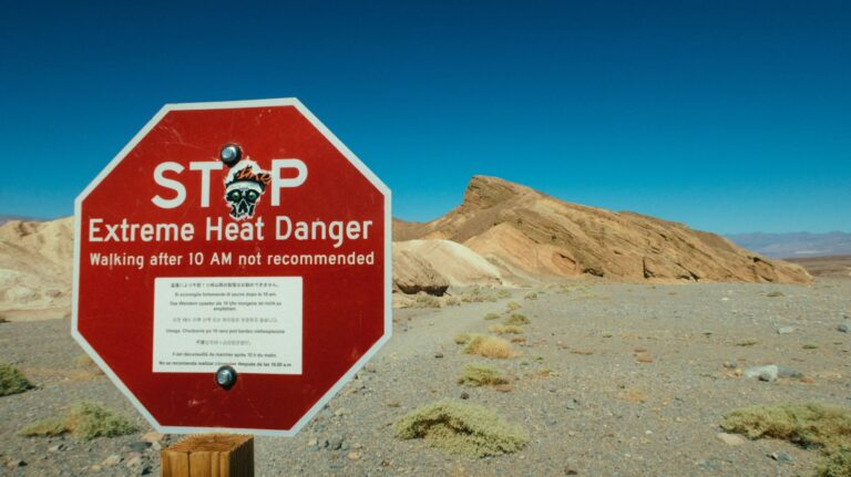 A red warning sign highlights extreme heat danger in a desert area.