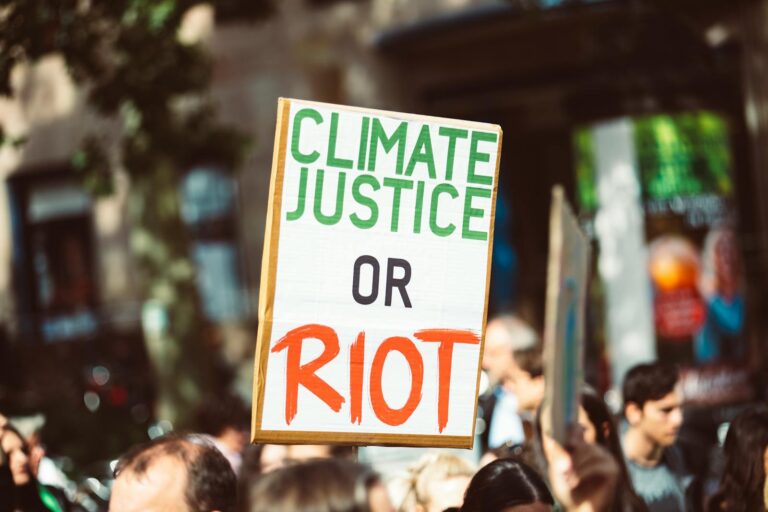 Close-up of a protest sign reading 'Climate Justice or Riot' in a street rally focused on climate change.