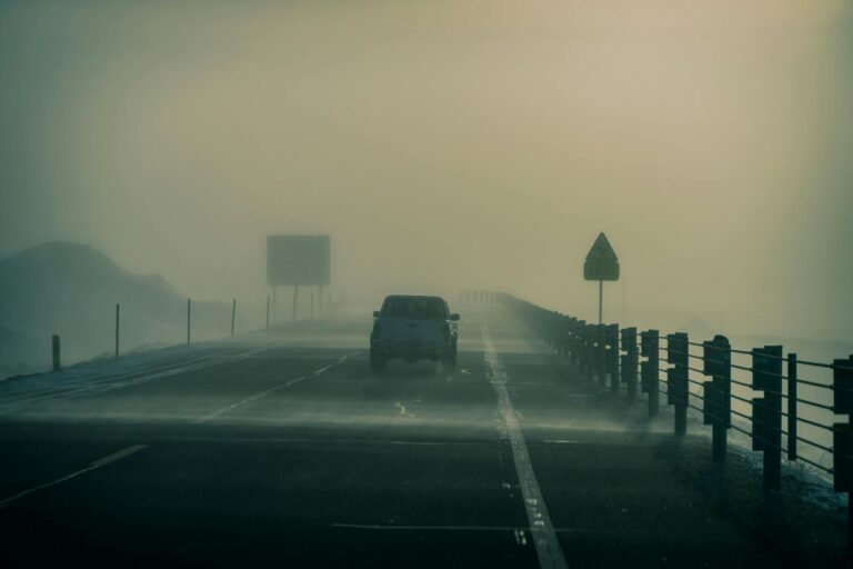 A car drives through dense fog on a misty road, creating an eerie and atmospheric scene.
