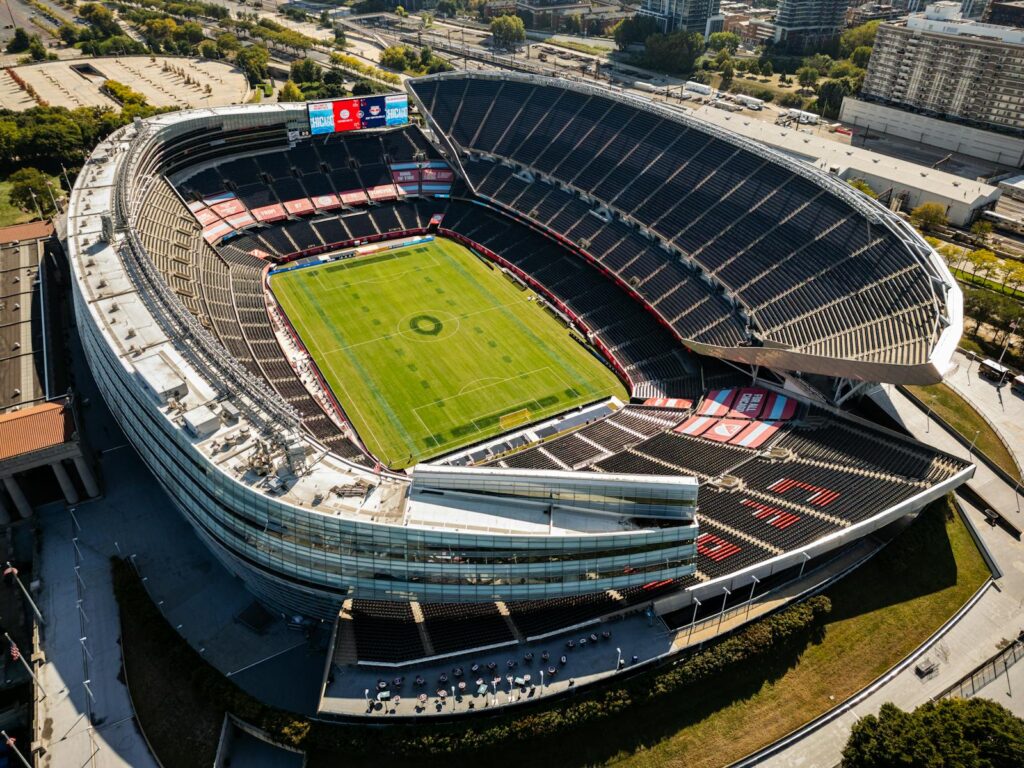 Aerial shot of a modern, empty soccer stadium surrounded by city buildings on a clear day.