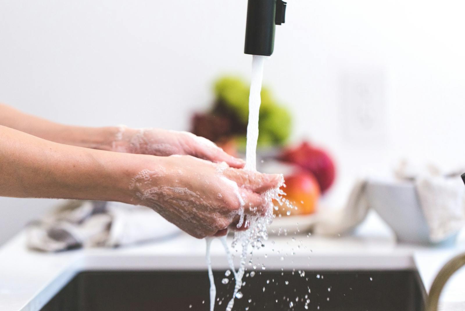 Hands being washed under a tap in a kitchen, promoting hygiene and cleanliness.