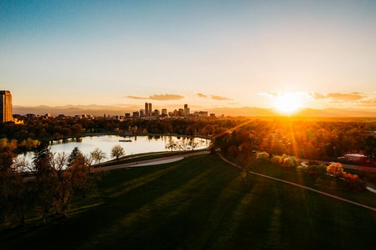Beautiful sunset landscape with a city skyline, serene lake, and expansive park.