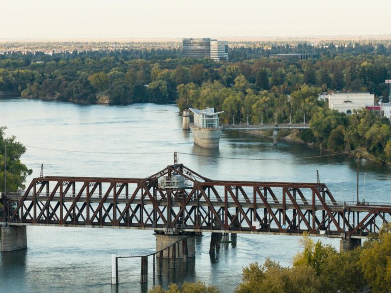 Aerial view of the scenic train bridge and river in Sacramento, California, surrounded by lush foliage.
