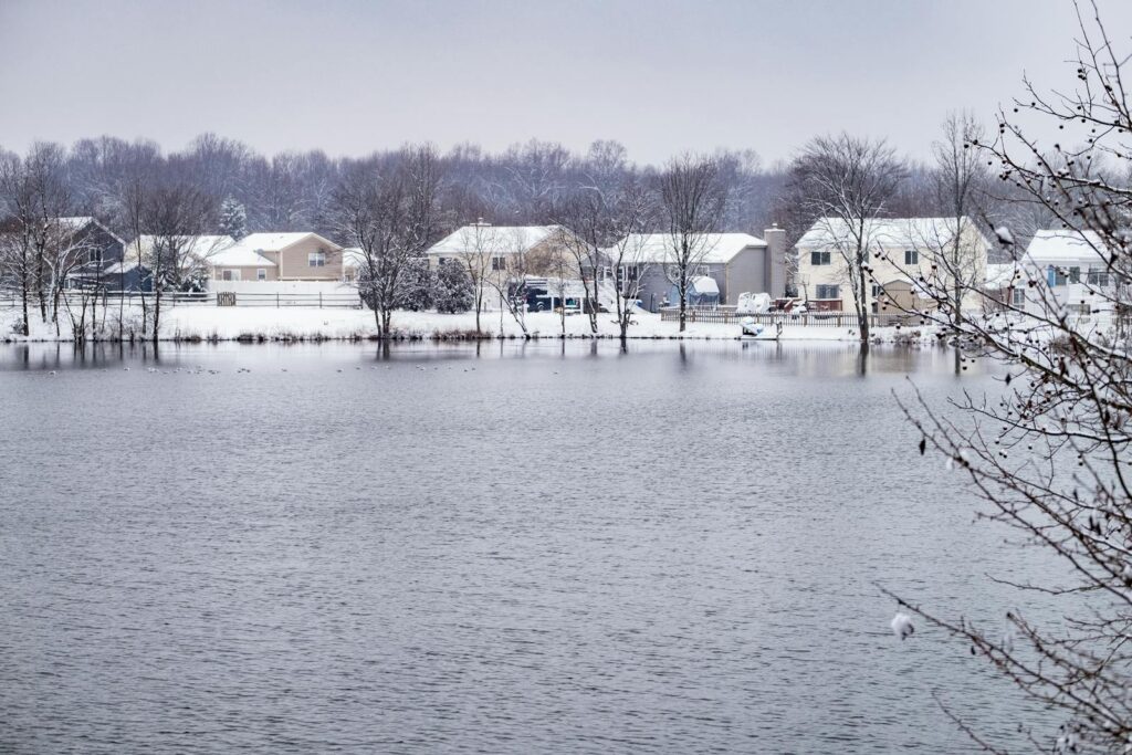 Picturesque snowy suburban scene by a calm pond in Maryland during winter.