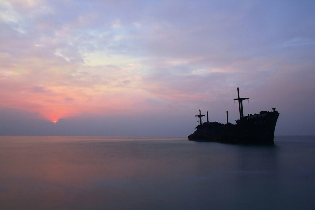 silhouette of person standing on rock formation in the middle of sea during sunset