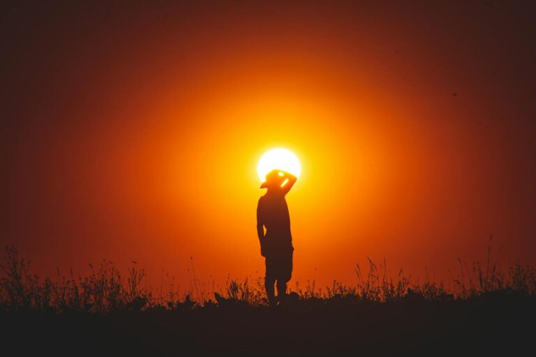 Person silhouetted against a vivid sunset sky in natural landscape.