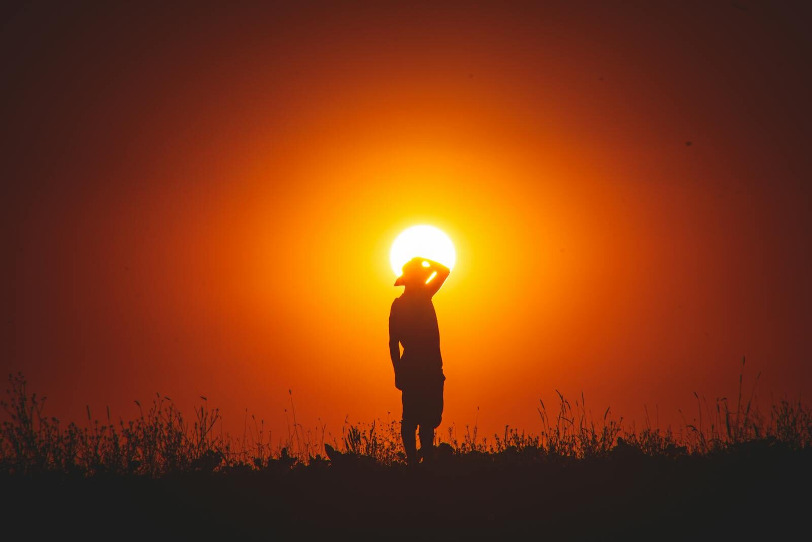 Person silhouetted against a vivid sunset sky in natural landscape.