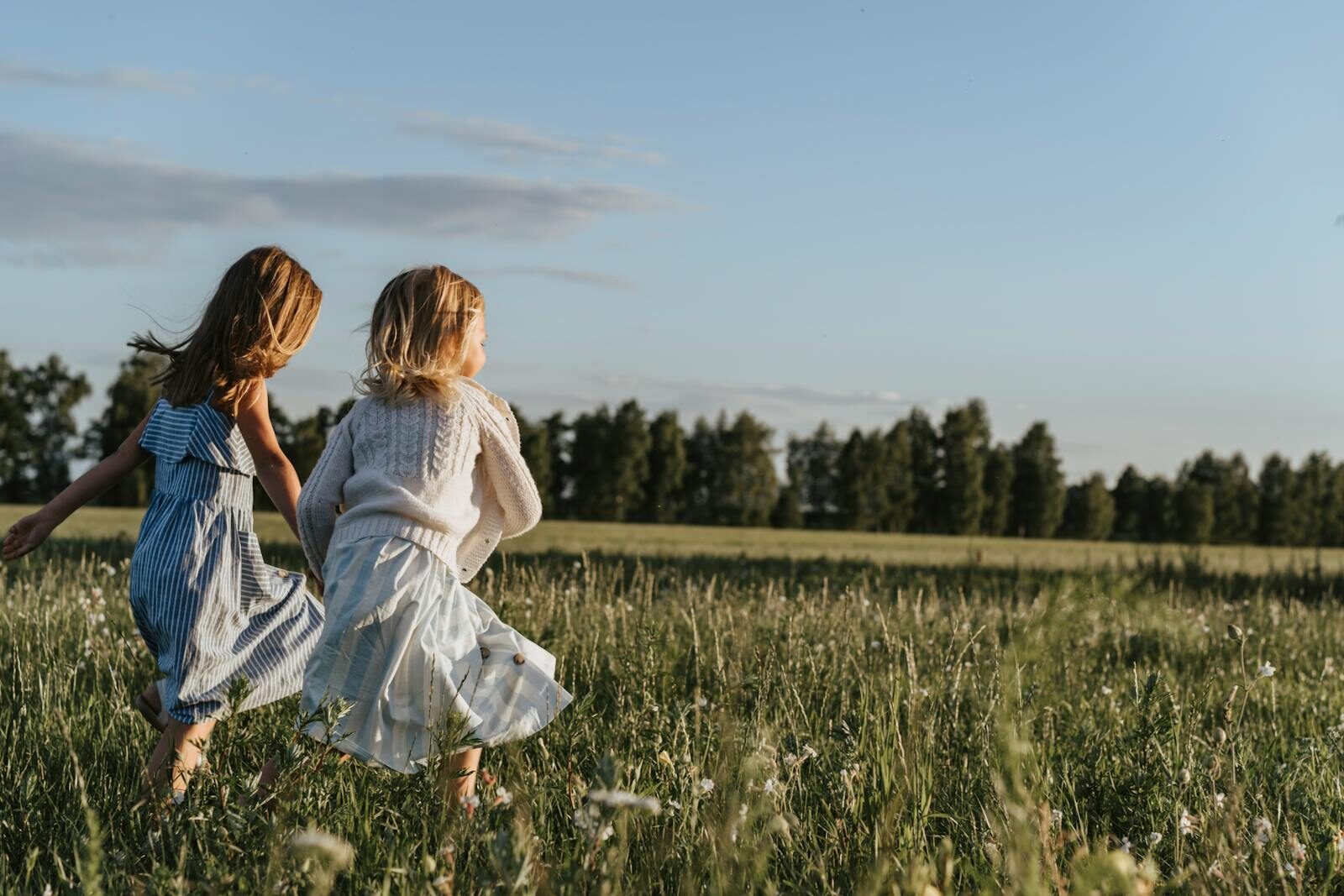 Two young girls joyfully running through a sunlit field, enjoying the outdoors.