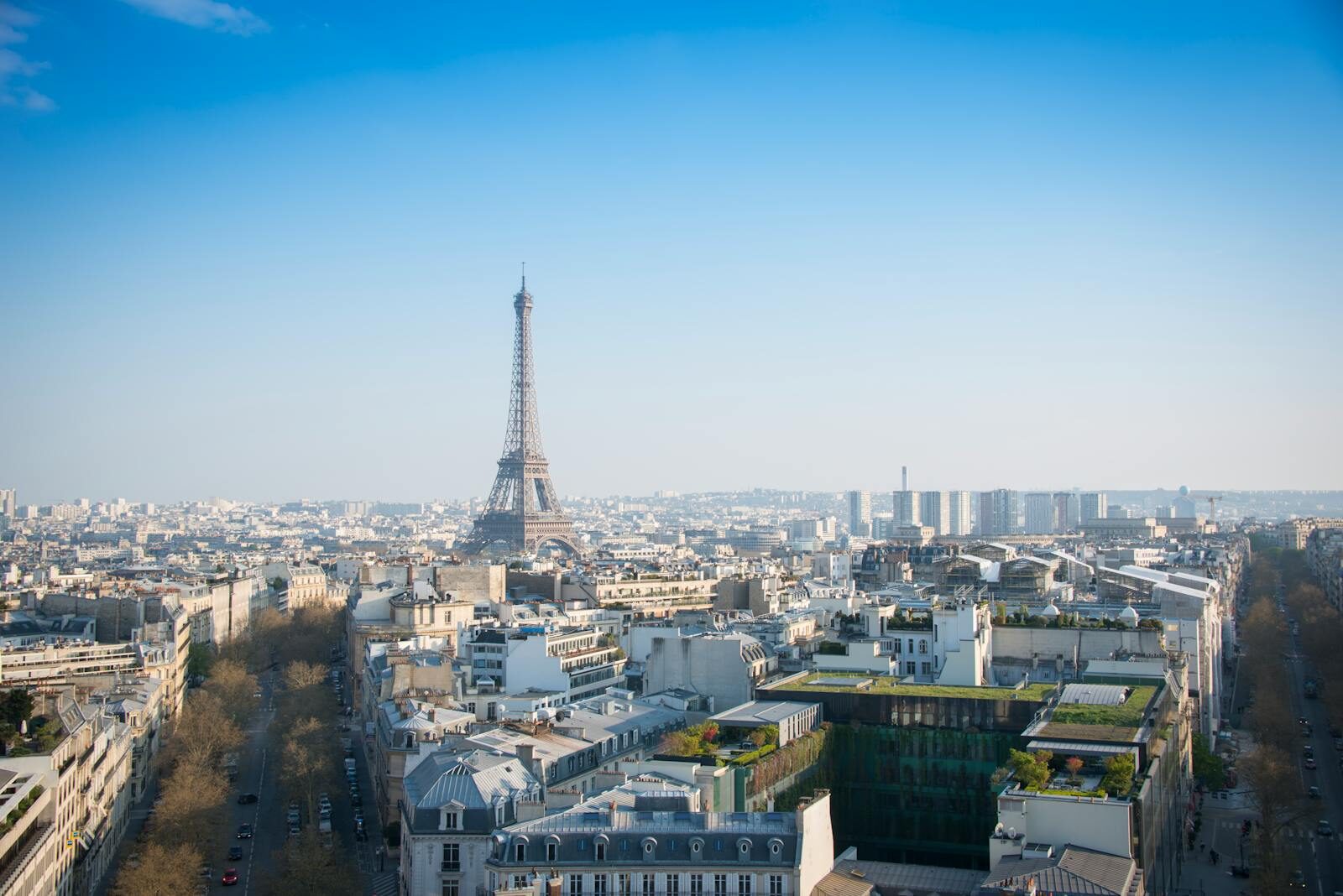 A stunning aerial view of Paris with the iconic Eiffel Tower and cityscape under a clear blue sky.