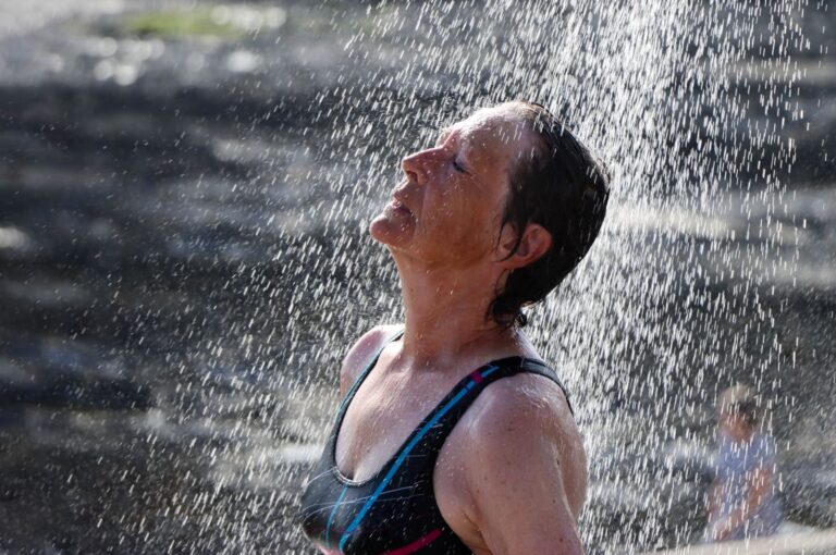 Woman enjoying a refreshing outdoor shower under a sunny sky, embracing nature.