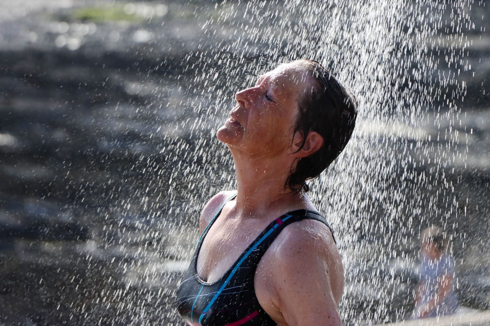 Woman enjoying a refreshing outdoor shower under a sunny sky, embracing nature.