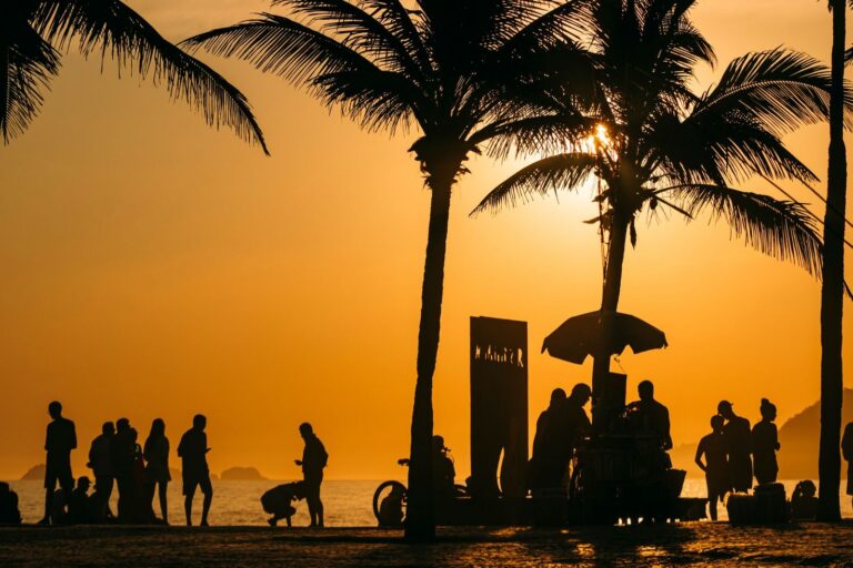 Silhouetted people and palm trees at sunset on a Rio de Janeiro beach, capturing the vibrant summer atmosphere.
