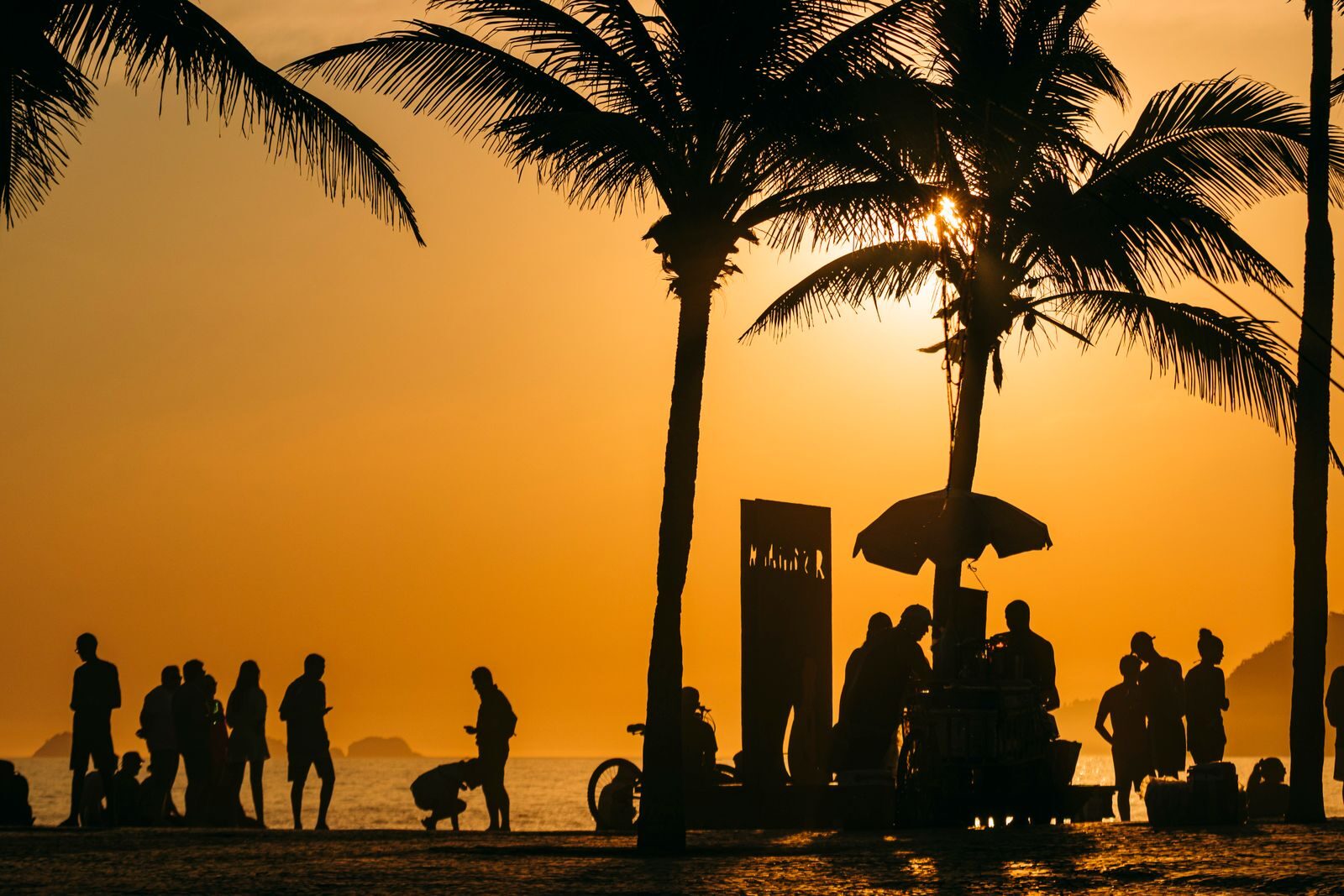 Silhouetted people and palm trees at sunset on a Rio de Janeiro beach, capturing the vibrant summer atmosphere.