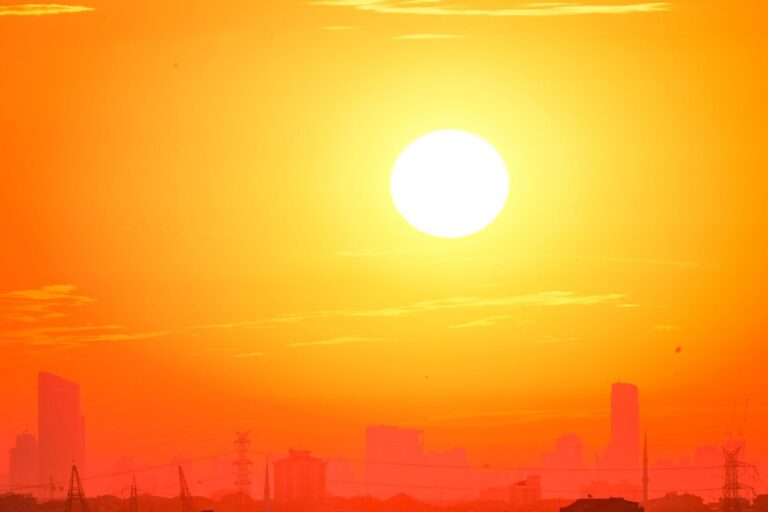 A city skyline silhouetted against a vivid, orange sunset sky.