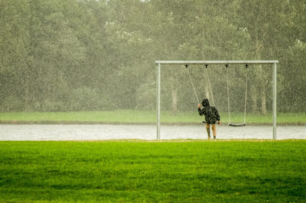 A child on a swing in a rainy park, capturing a serene moment with falling rain.