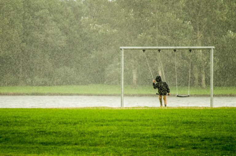 A child on a swing in a rainy park, capturing a serene moment with falling rain.