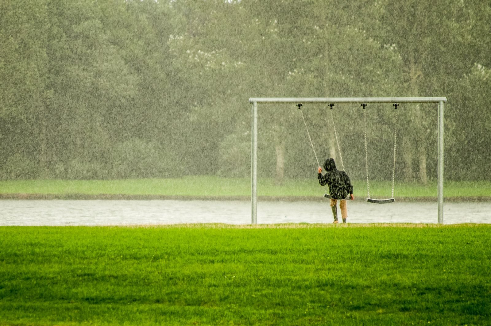 A child on a swing in a rainy park, capturing a serene moment with falling rain.