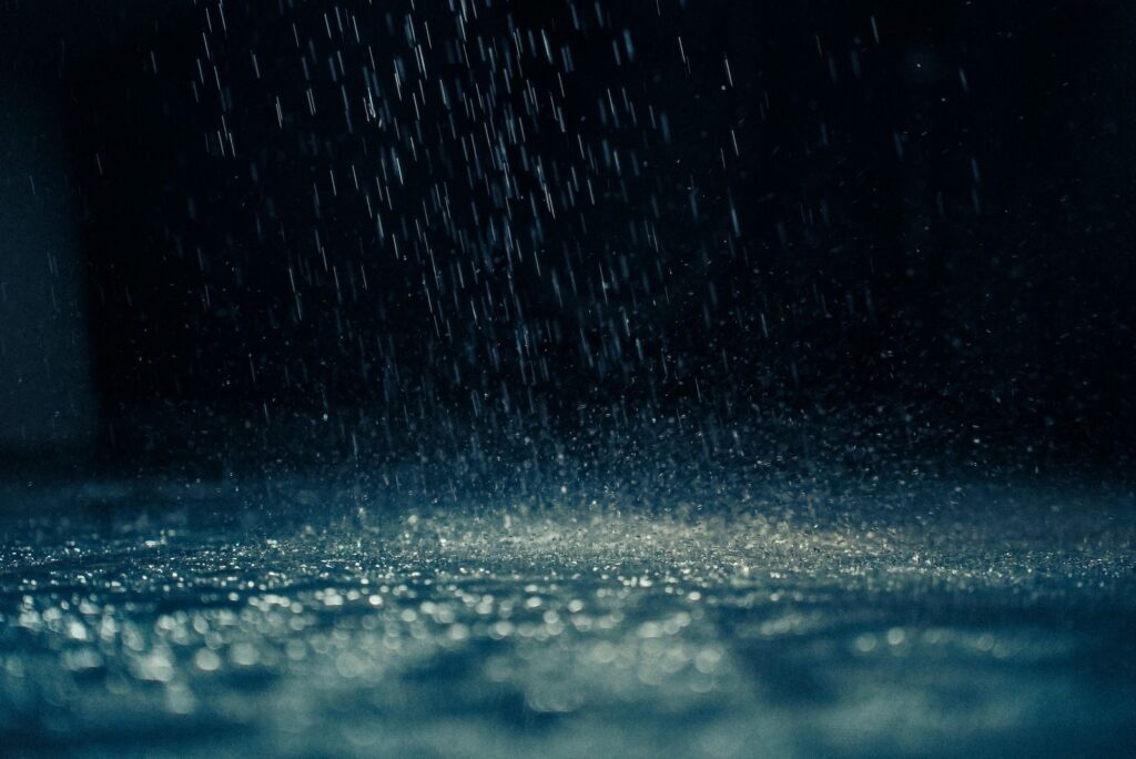 Dramatic close-up of rain droplets falling on a dark surface, capturing movement and reflections.