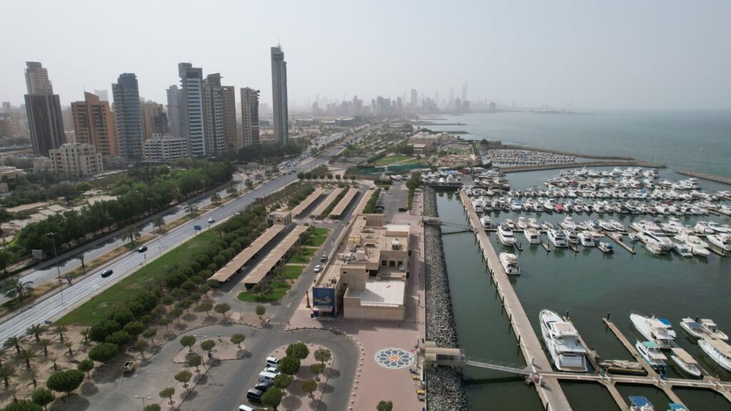 Aerial view of Kuwait City's modern skyline and bustling harbor with yachts.