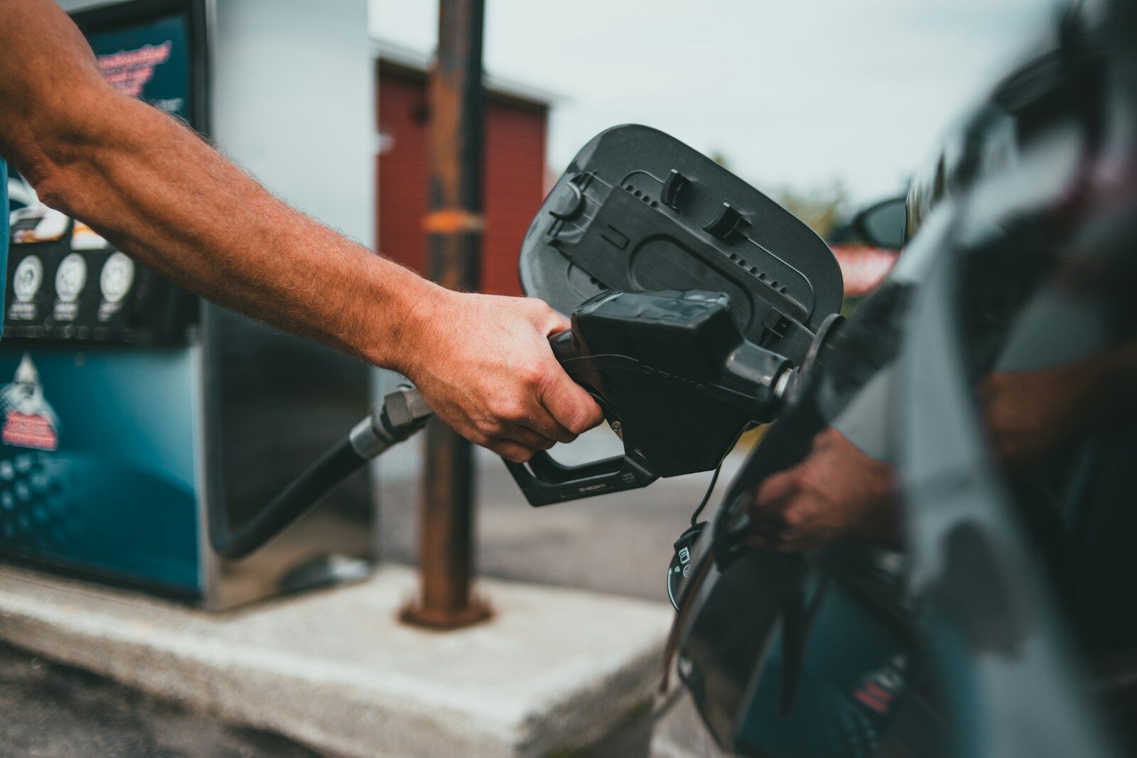 A person holding a black fuel nozzle to a car at a gas station