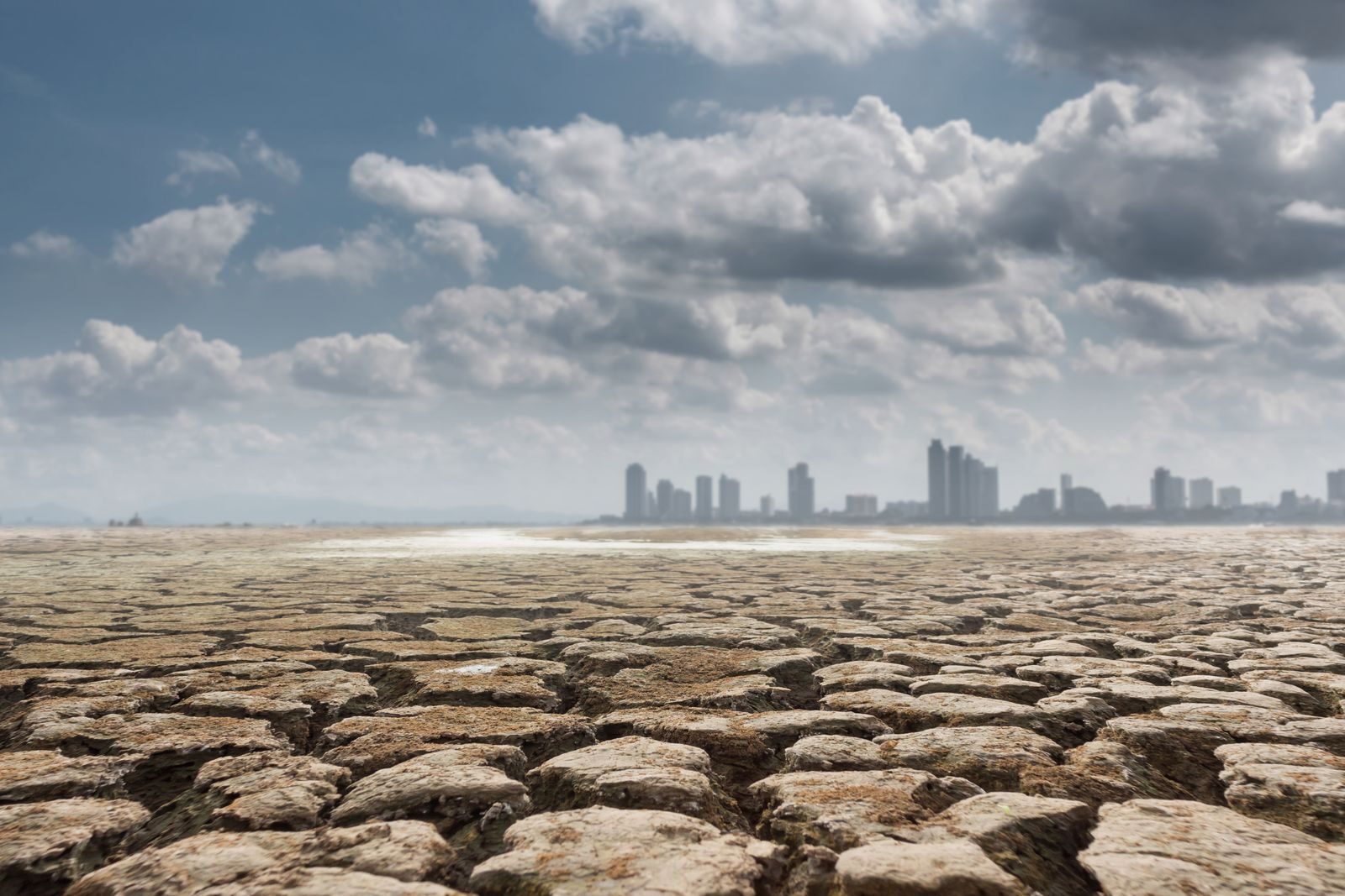 Vast territory of dried soil with contemporary buildings and skyscrapers on background on cloudy sunny day