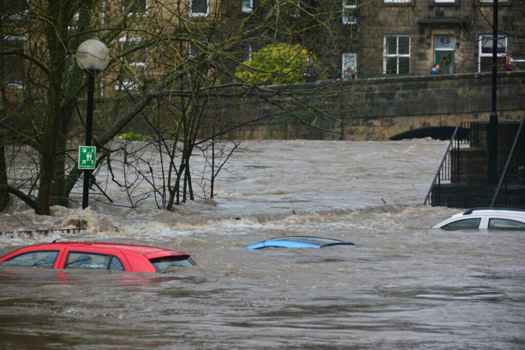 Three cars partially submerged in a flooded river near a stone bridge