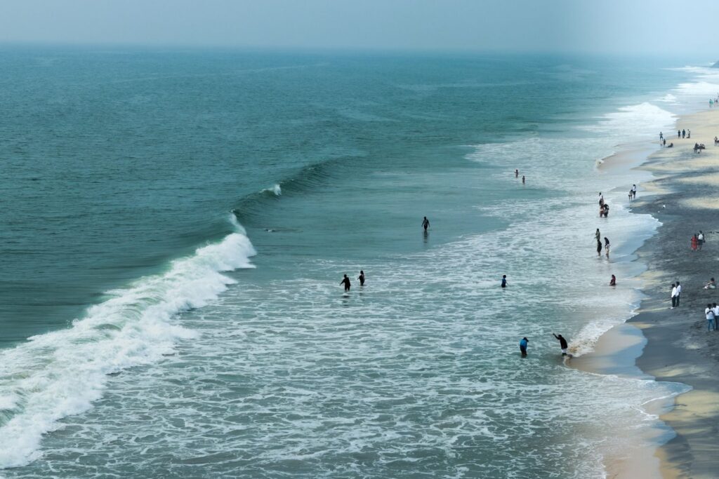 People enjoying a sunny day by the waves on a Kerala beach.