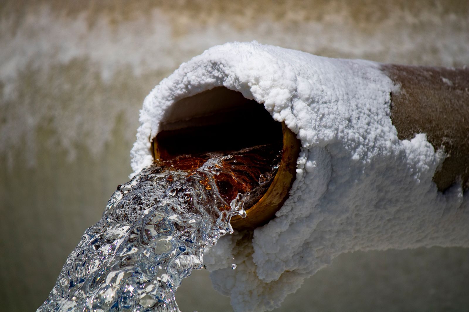 Close-up of water flowing from a rusty pipe with salt deposits, capturing motion and texture.