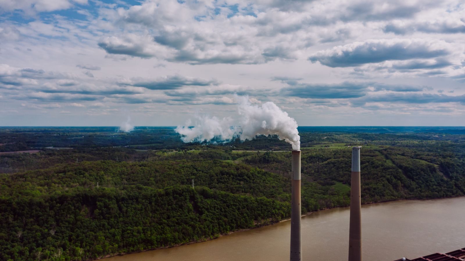 From above drone view of pipes of factory located near river emitting harmful substances into atmosphere