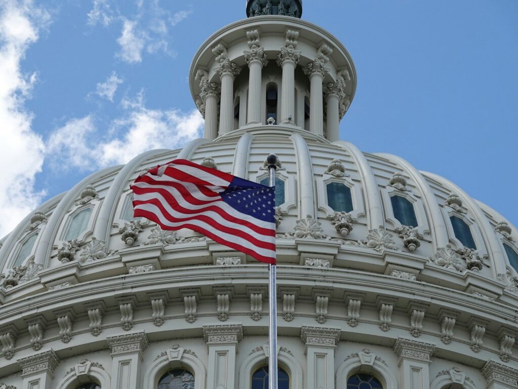 The United States flag waving before the white dome of the Capitol building